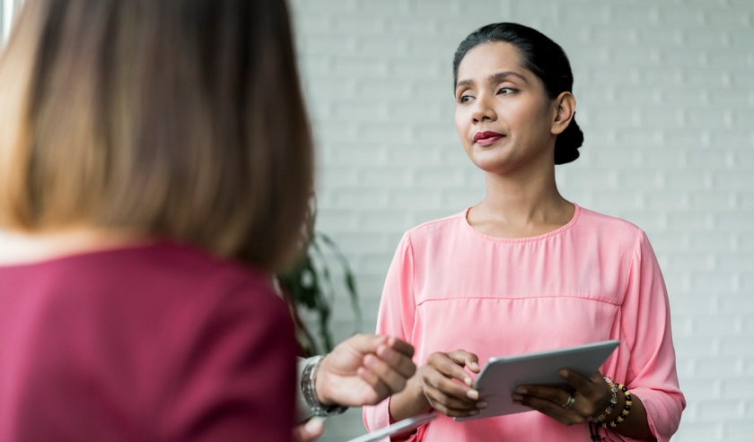 Woman holding a tablet device, while in discussion with others