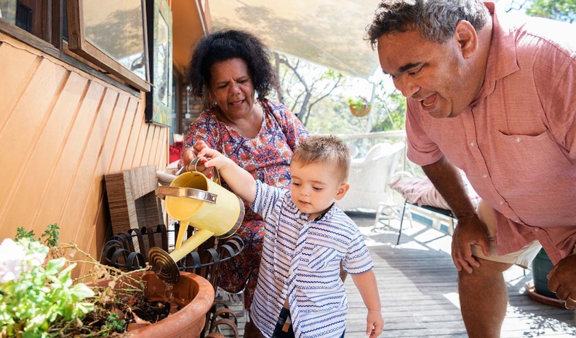 Aboriginal family in garden, boy holding watering can, grandmother and grandfather watching