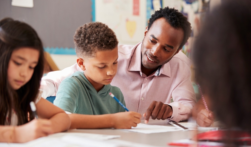 Male teacher working with elementary school boy at his desk