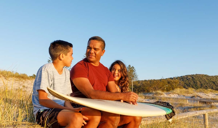 Dad with kids and a surfboard at the beach