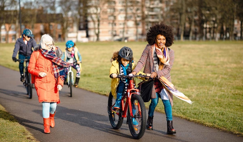 Three generation family walking through a public park. The little boy is cycling through the park with his mothers assistance while she talks to her mother in-law.