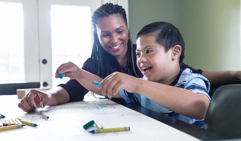 Little boy with Down Syndrome colors with his mom in their home.