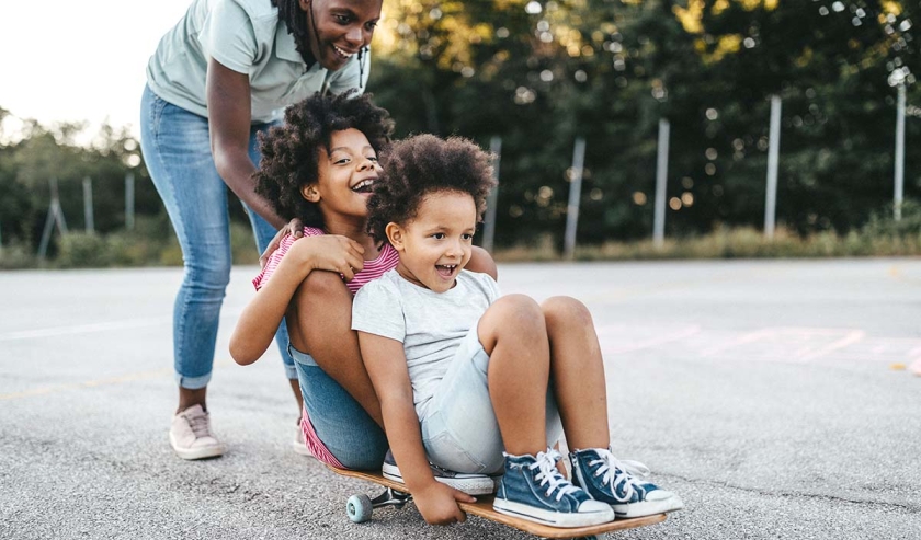 Mother and daughters having fun riding skateboard on playground