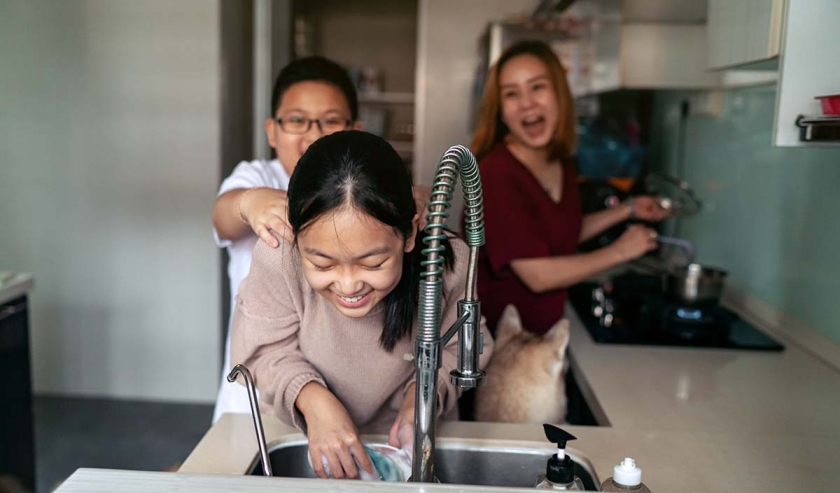 Asian mother and her preteen kids having fun while doing house chores together