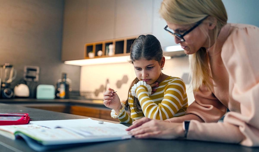Adult helping girl with schoolwork in the kitchen