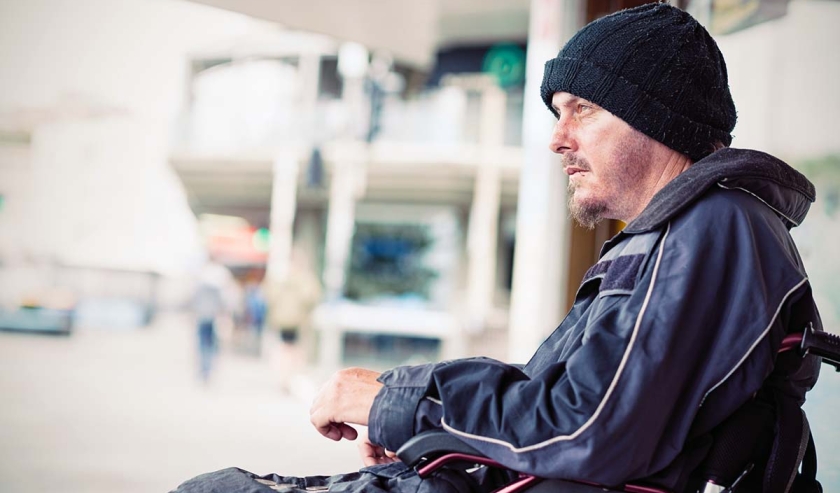 Homeless young invalid man sitting in wheelchair on the street