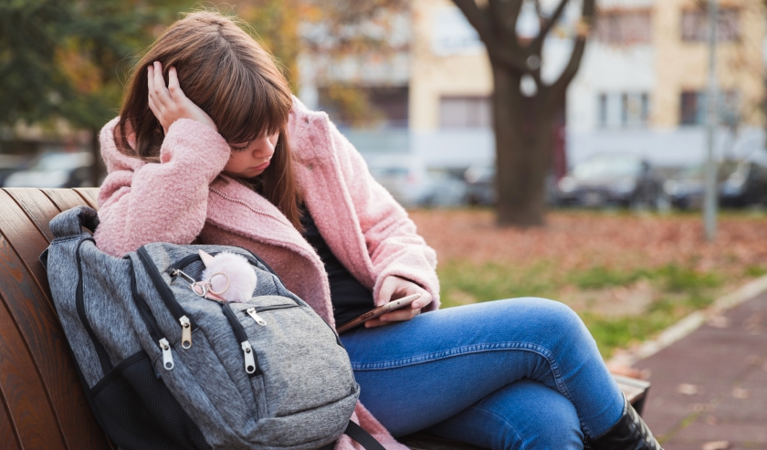 Nervous girl leaning onto a school bag and text messaging outdoor