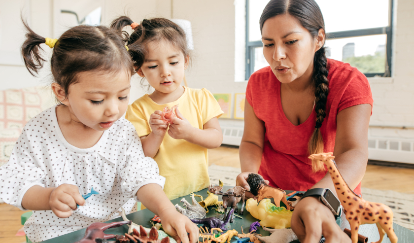 Two young girls and a female carer playing with toy animals