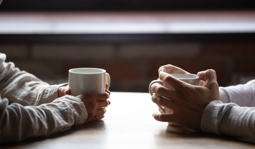 Two sets of hands clutching mugs, on a table
