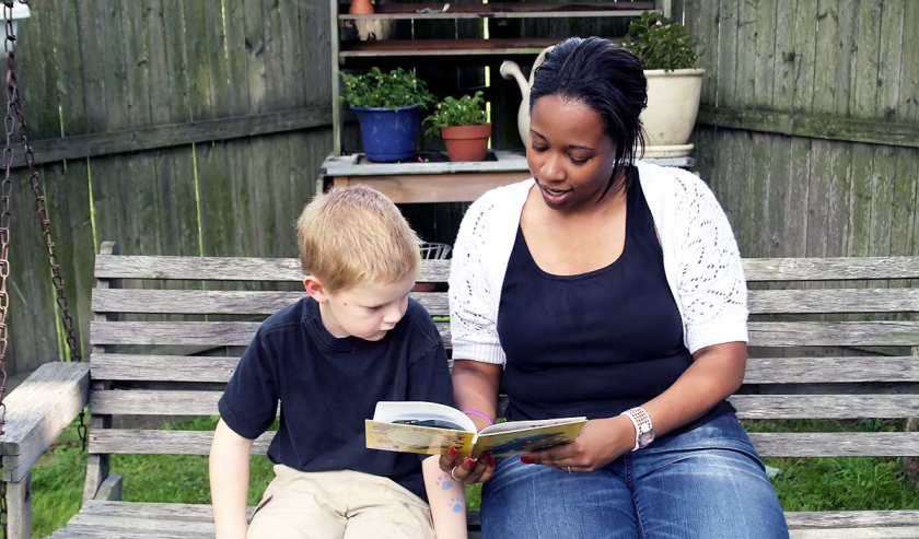 Woman reading to a young child sitting together outside on a bench
