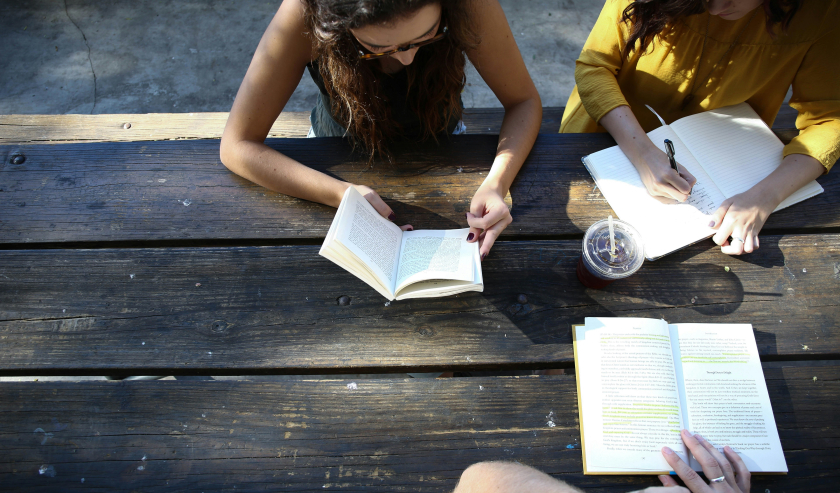 Young women discussing books at an outside table
