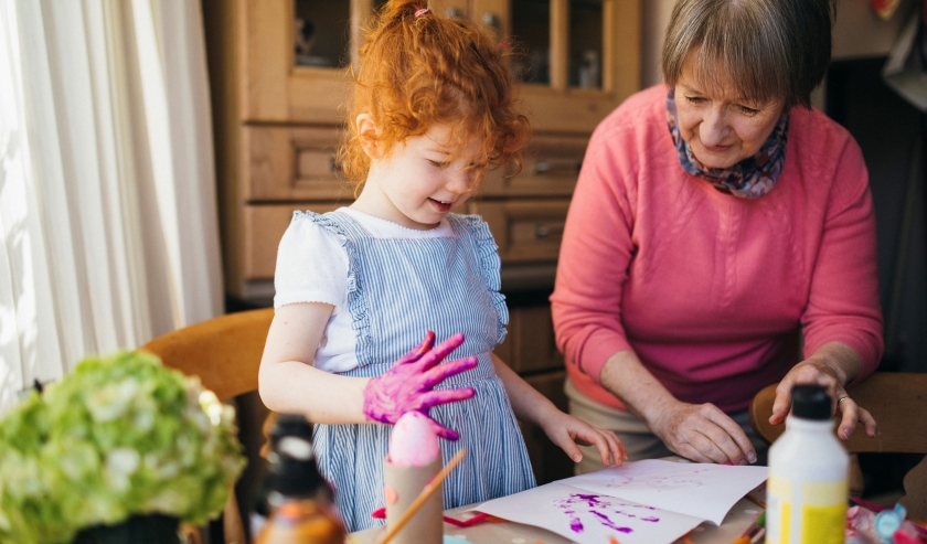 Young child playing with paint, supervised by an older female adult