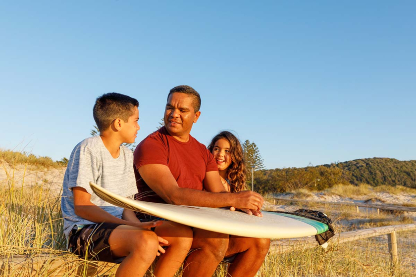 Dad with kids and a surfboard at the beach