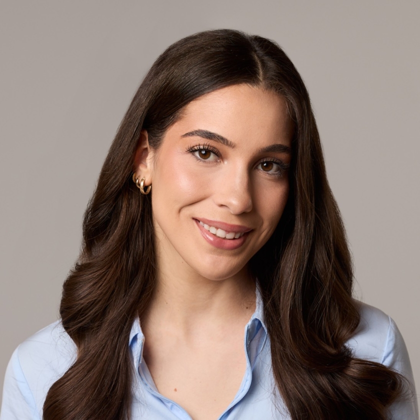 Anastasia has long, wavy dark brown hair. Anastasia is wearing a zip-up shirt in the colour baby blue.