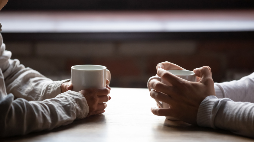 Two sets of hands clutching mugs, on a table