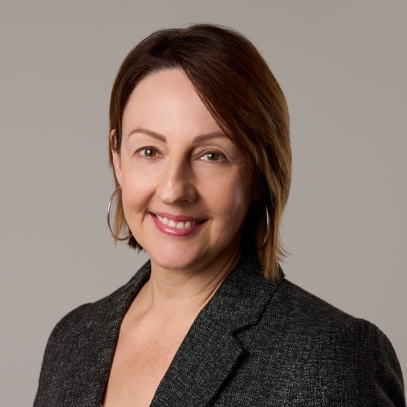 Melinda has straight, shoulder length dark brown hair. Melinda is wearing a dark grey blazer.