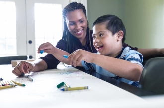 Little boy with Down Syndrome colors with his mom in their home.